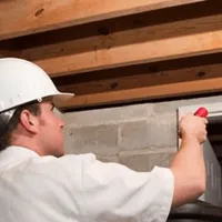 Termite inspection technician checking a basement wall and framing for termite activity in Arvada, CO